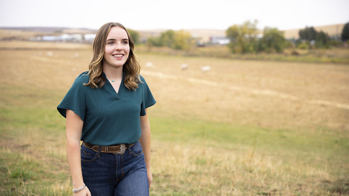 A woman walks in a pasture with cows in the background.