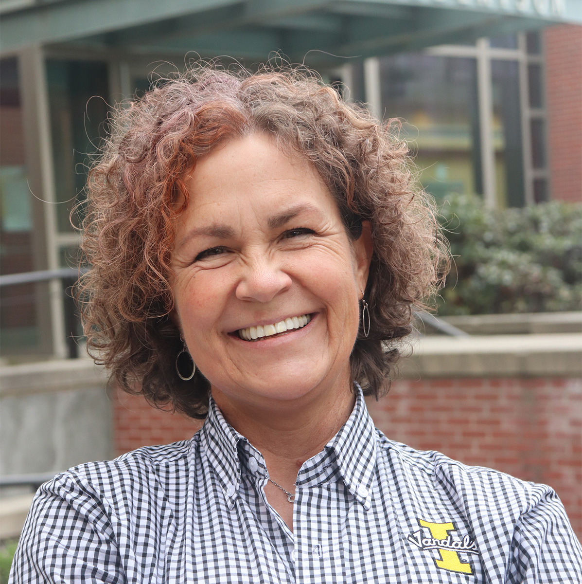 Lori Rock smiles outdoors with brick buildings in the background