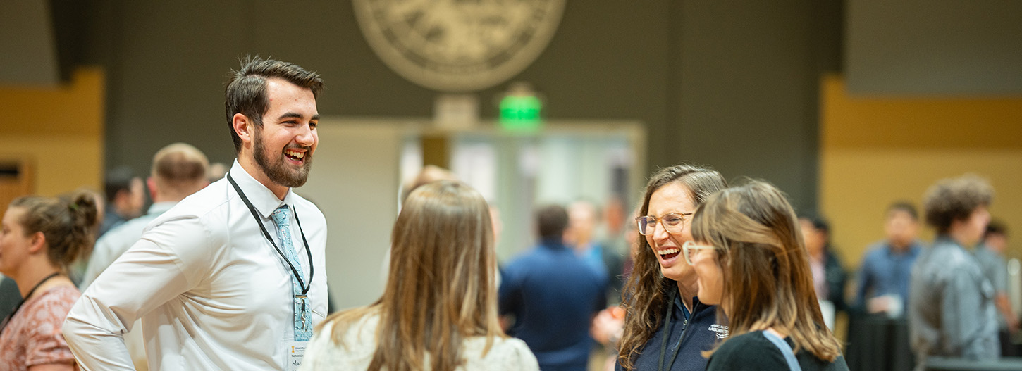 Man and three women in business clothes laughing and chatting amongst each other.