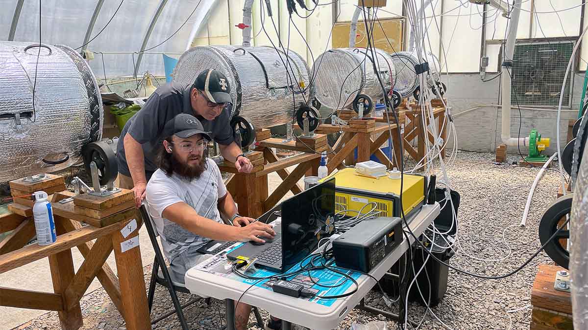 Two men look at a computer in a room with dairy manure composters.