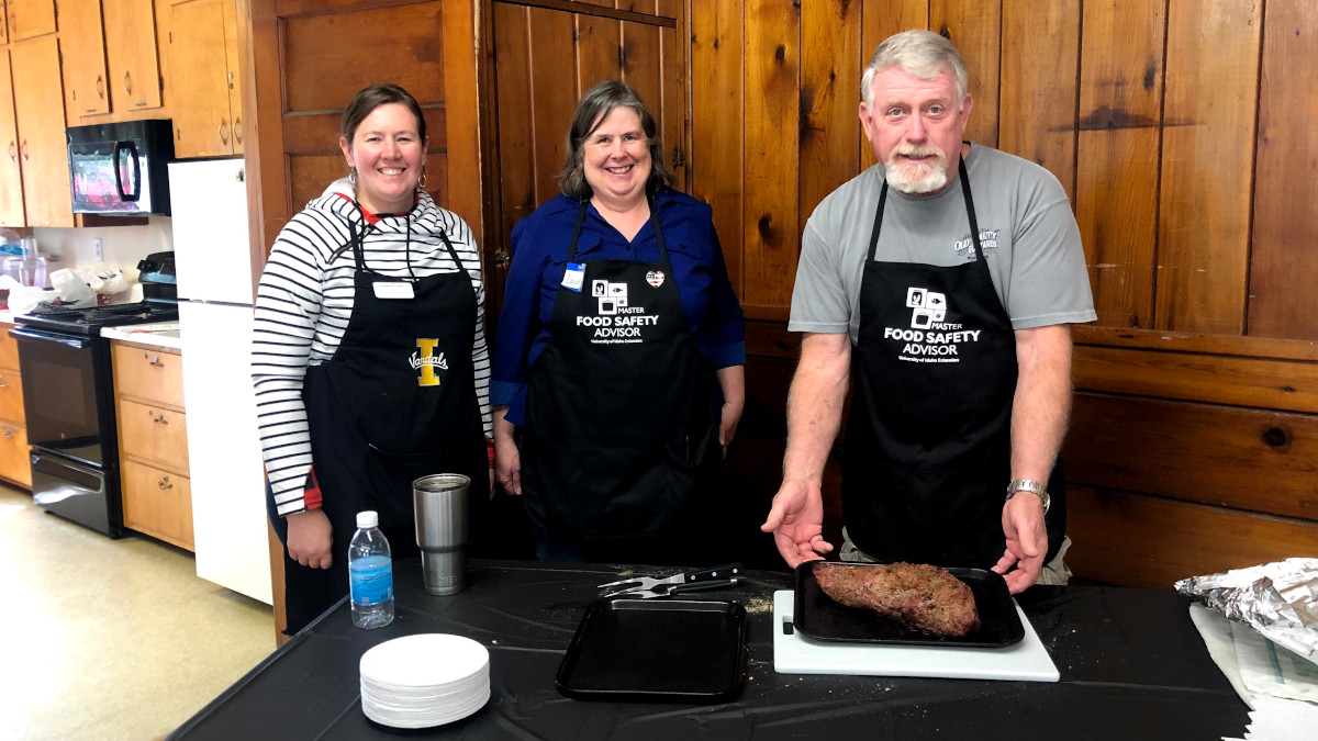 Three people stand in front of table with roast.