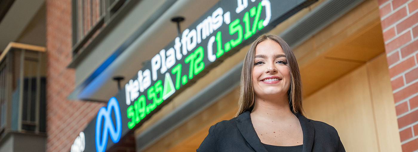 Woman stands in front of market price LED ticker display board.