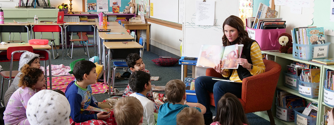 Woman holding book and reading to group of children.