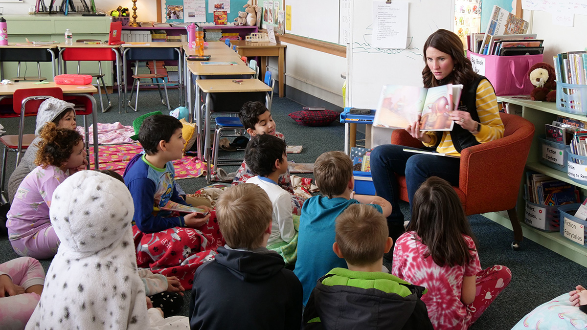 Woman holding book and reading to group of children.