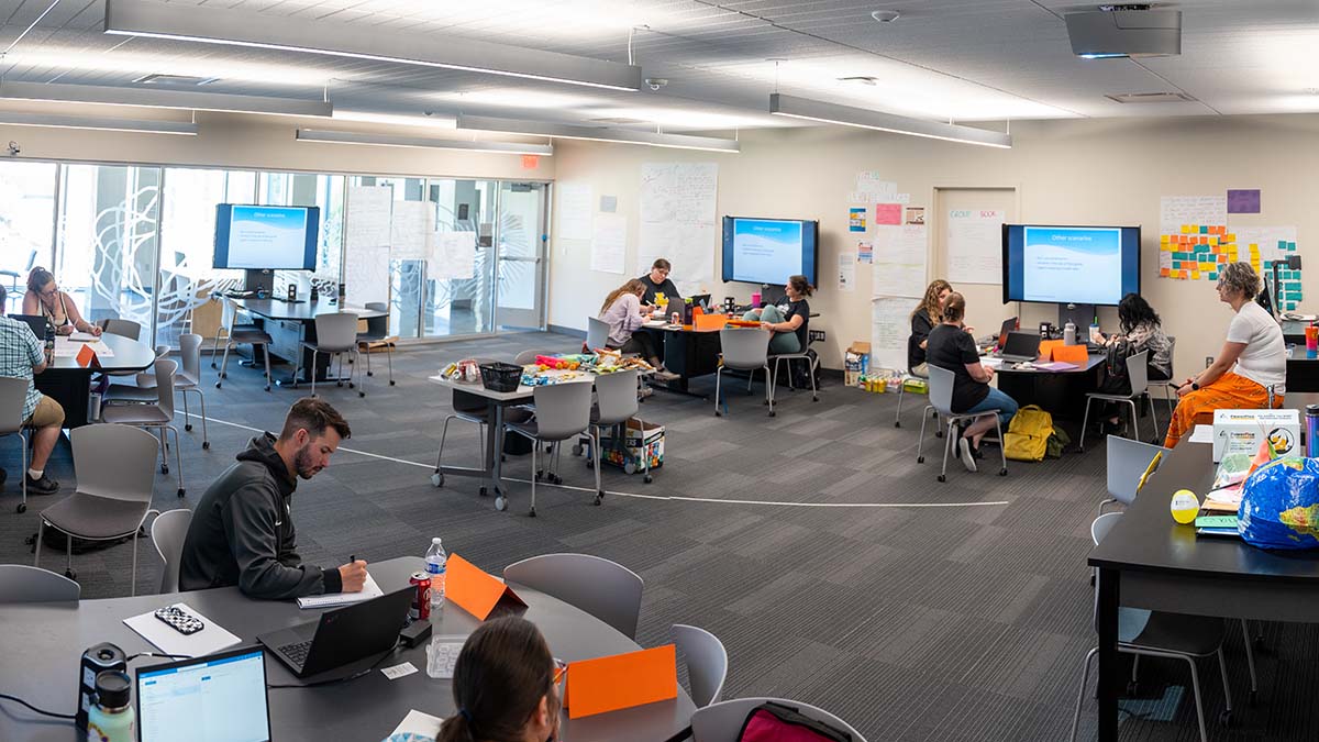 Instructor sitting on desk while students are working on projects.