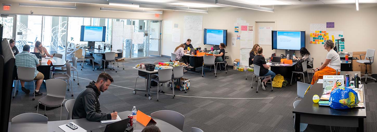 Instructor sitting on desk while students are working on projects.