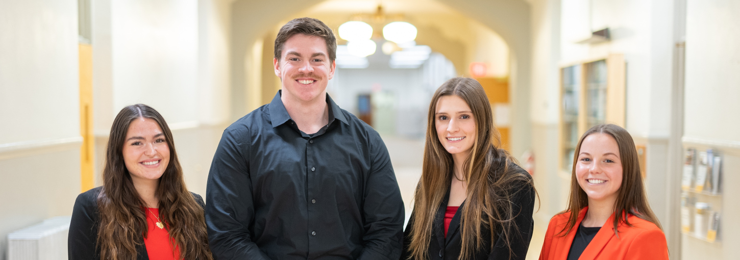 Four students standing next to each other in Admin Building hallway.