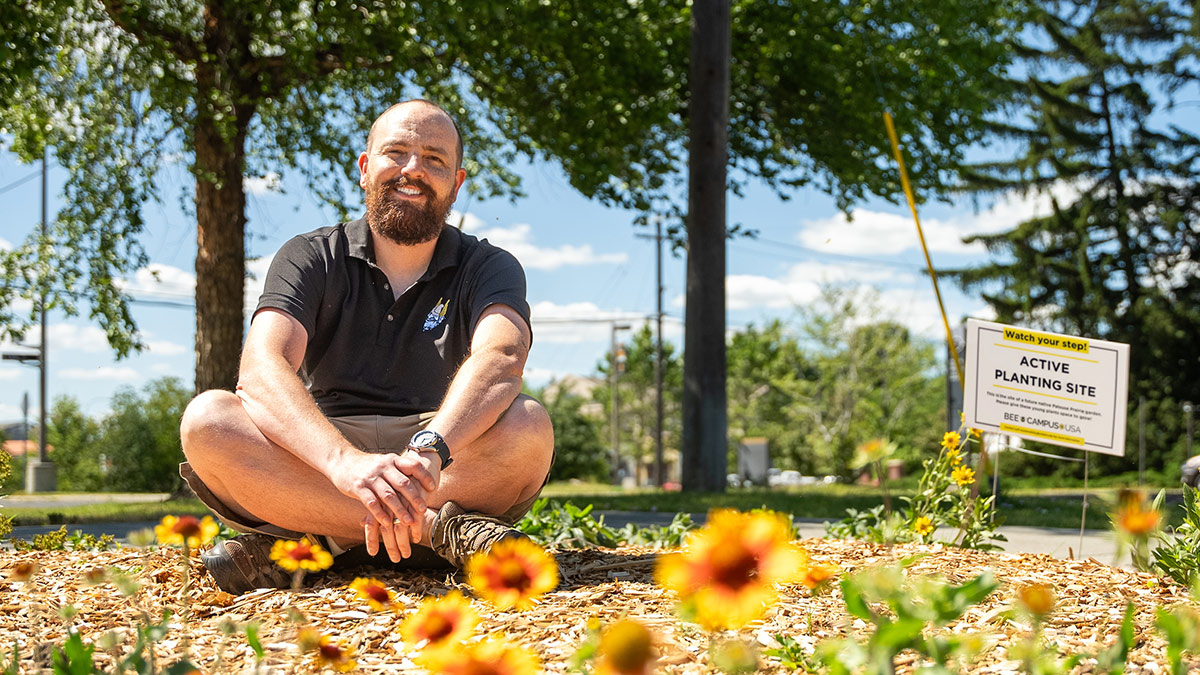 Karl Meyer sits on the ground, next to a patch of yellow flowers.