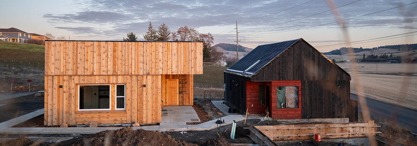 Two small houses in front of a field and mountain.