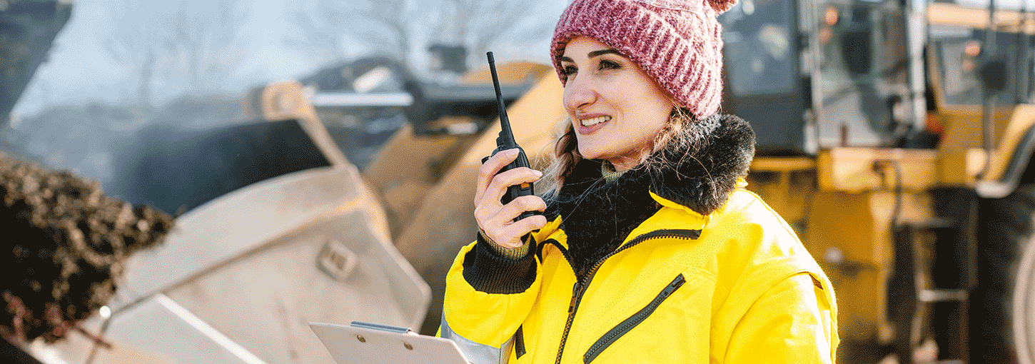 A student talks into a walkie talkie. A bulldozer hauls compost in the background.